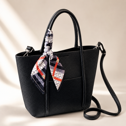Black handbag with a patterned scarf draped over the handle on a beige background