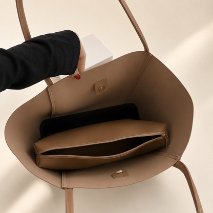 Brown handbag with a compartment open, showing a black item inside, on a beige background.