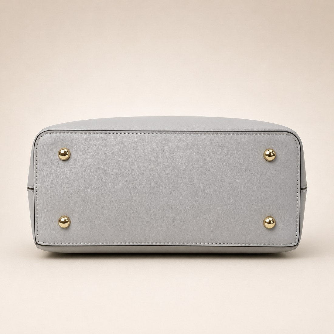 Light gray handbag with gold studs on a beige background