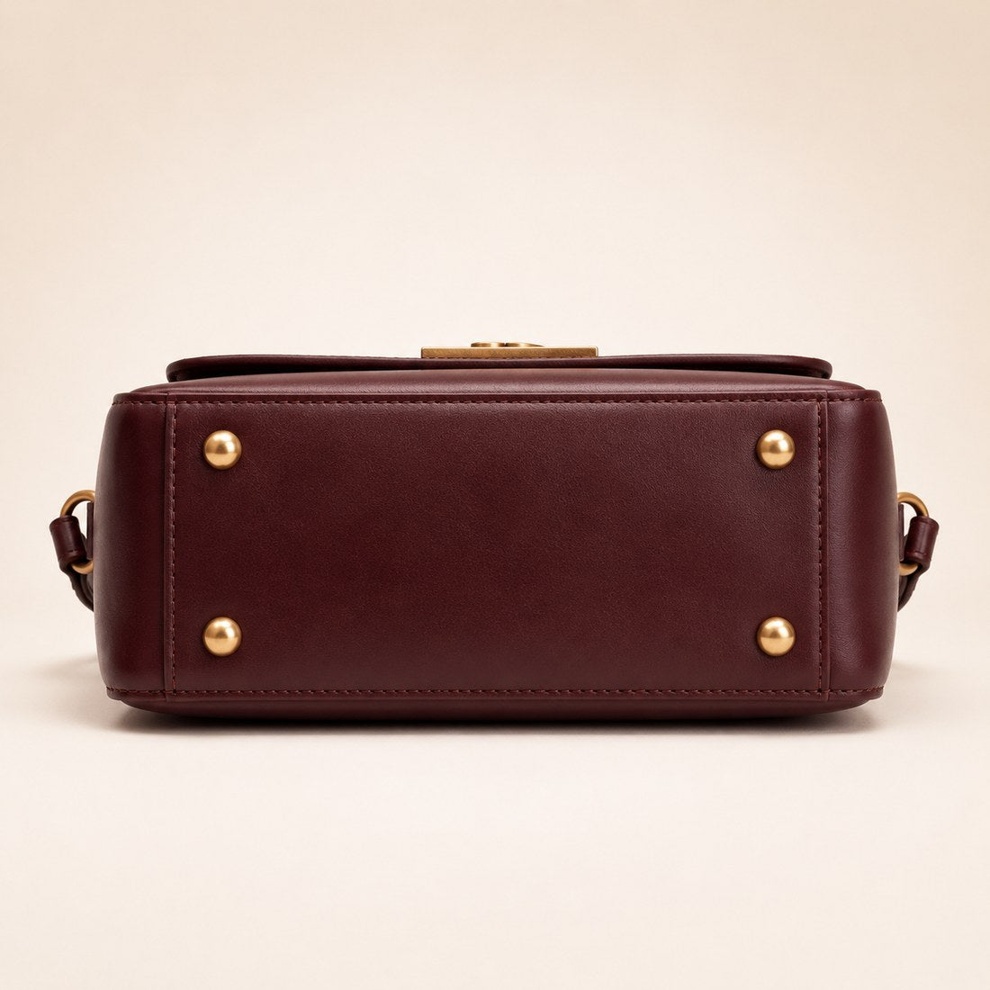 Brown leather handbag with gold accents on a beige background